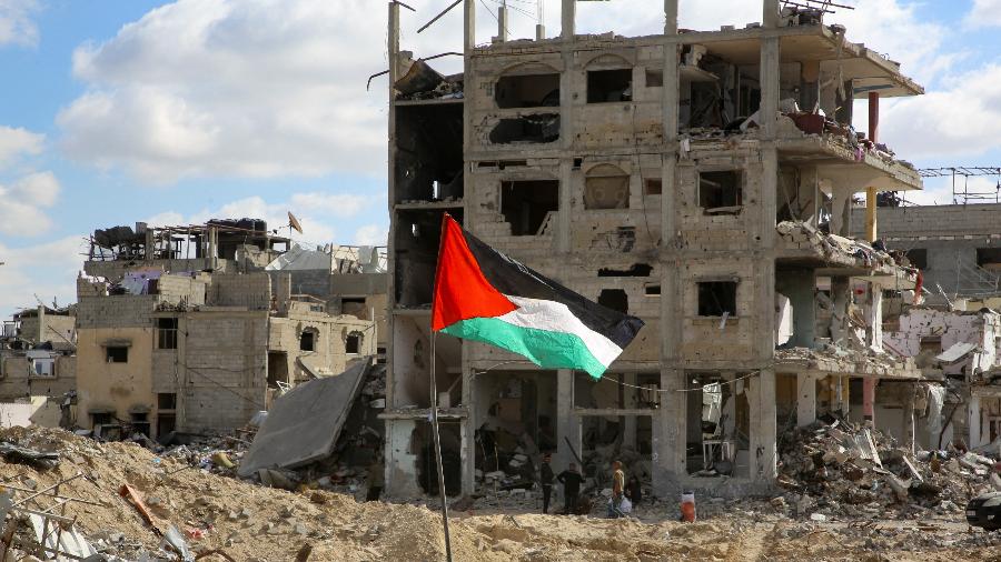 Bandeira palestina é vista nesta segunda (20) fincada diante de escombros de casas destruídas por bombardeios israelenses em Rafah, no sul da Faixa de Gaza - Hatem Khaled / Reuters