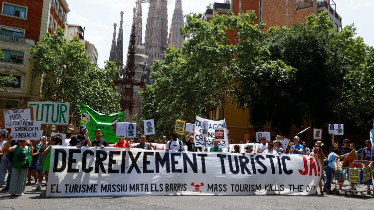 15.jun.2025 - Pessoas seguram uma faixa com os dizeres "reduza o turismo agora" durante um protesto contra o turismo em massa, em Barcelona 15.jun.2025 - Pessoas seguram uma faixa com os dizeres "reduza o turismo agora" durante um protesto contra o turismo em massa, em Barcelona