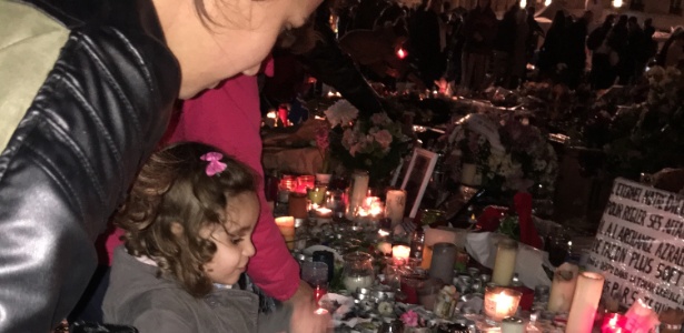 A portuguesa Cíntia de Oliveira ajuda a filha de 2 anos e meio a acender uma vela em homenagem às vítimas, no memorial da praça da República, em Paris - Carolina Vila-Nova/UOL