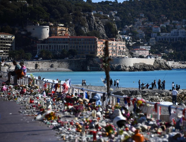 Franceses sentam ao lado de velas, flores e bandeiras colocados na orla da praia em homenagem às vítimas do ataque terrorista em Nice, na França, em 14 de julho - Anne-Christine Poujoulat