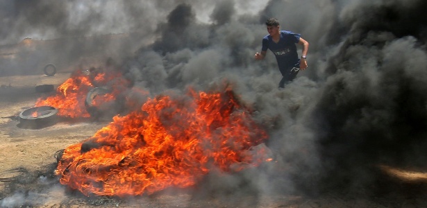 14.mai.2018 - Homem palestino caminha em meio a fumaça de pneus em chamas durante confronto com forças de Israel na cidade de Khan Yunis, na Faixa de Gaza. Palestinos protestam contra a inauguração da embaixada dos EUA em Jerusalém - Said Khatin/AFP