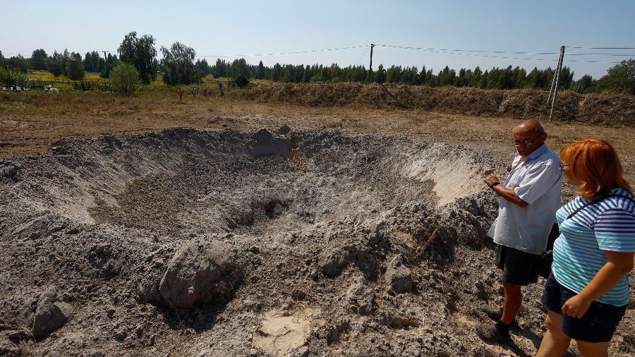 Ucraniano observam cratera nos arredores de Kiev após ataque russo neste domingo (18)