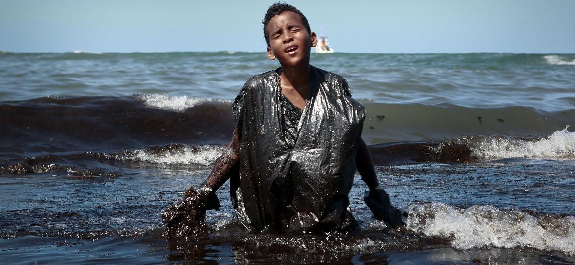 Menino coberto de óleo deixa água na praia de Cabo de Santo Agostinho (PE) - Leo Malafaia/AFP