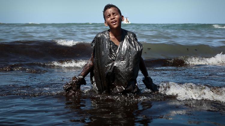 21.out.2019 - Menino coberto de óleo deixa água na praia de Cabo de Santo Agostinho (PE) - Leo Malafaia/AFP - Leo Malafaia/AFP