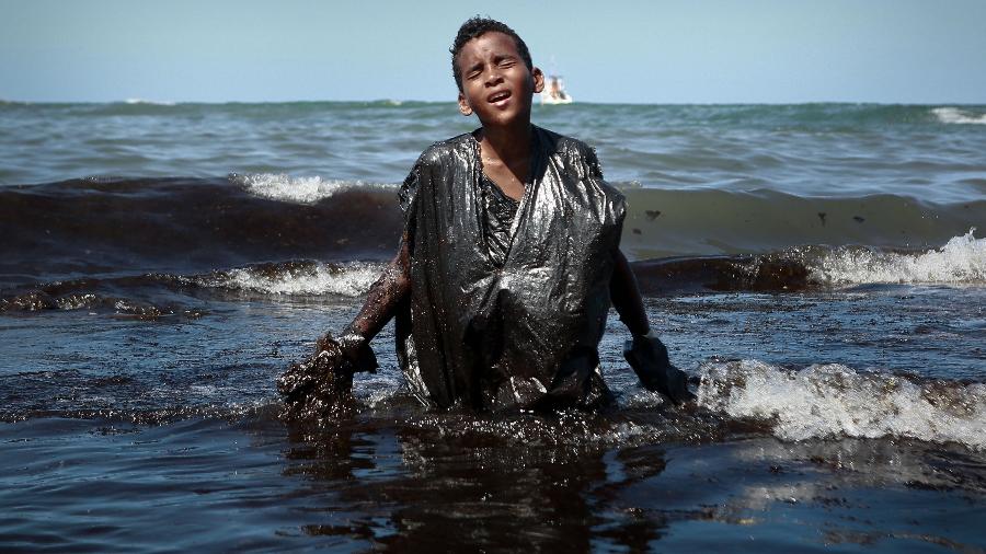 Menino coberto de óleo deixa água na praia de Cabo de Santo Agostinho (PE) - Leo Malafaia/AFP