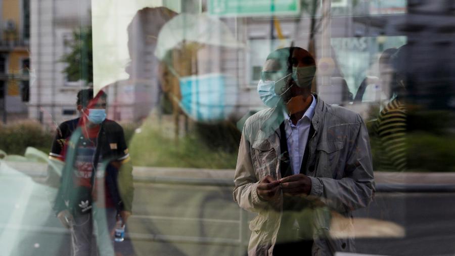 A imagem de um homem que espera em um ponto de ônibus é refletida em uma janela de ônibus, enquanto o país facilita o bloqueio devido à disseminação da doença por coronavírus (COVID-19), na estação Cais do Sodre, em Lisboa, Portugal - RAFAEL MARCHANTE/REUTERS