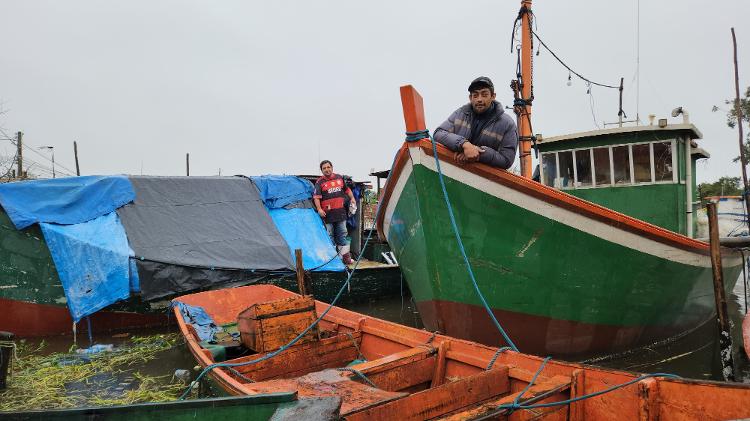 23.mai.2024 - Pescadores Rodrigo Machado (esq.) e Eduardo Santos (dir.) atracados em barcos em Pelotas (RS)