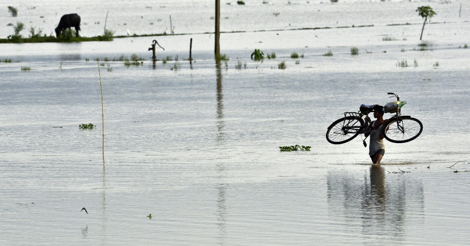 21.ago.2015 - Jovem carrega bicicleta em uma área inundada de Morigaon, na Índia