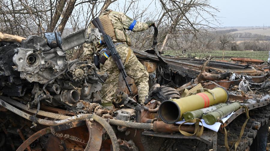 01.abr.2022/ Um soldado ucraniano verifica os destroços de um tanque russo queimado fora da vila de Mala Rogan, a leste de Kharkiv - SERGEY BOBOK / AFP