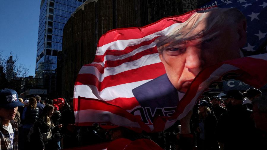 Bandeira com a imagem de Trump é carregada por apoiadores em comício em Nova York