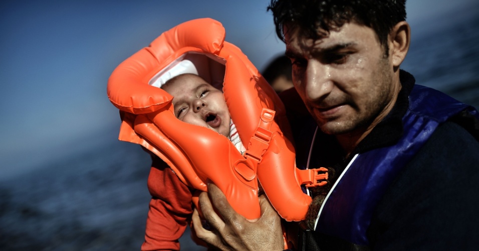 5.out.2015 - Migrante segura bebê com colete salva-vidas ao chegar à ilha grega de Lesbos após travessia marítima saindo da Turquia