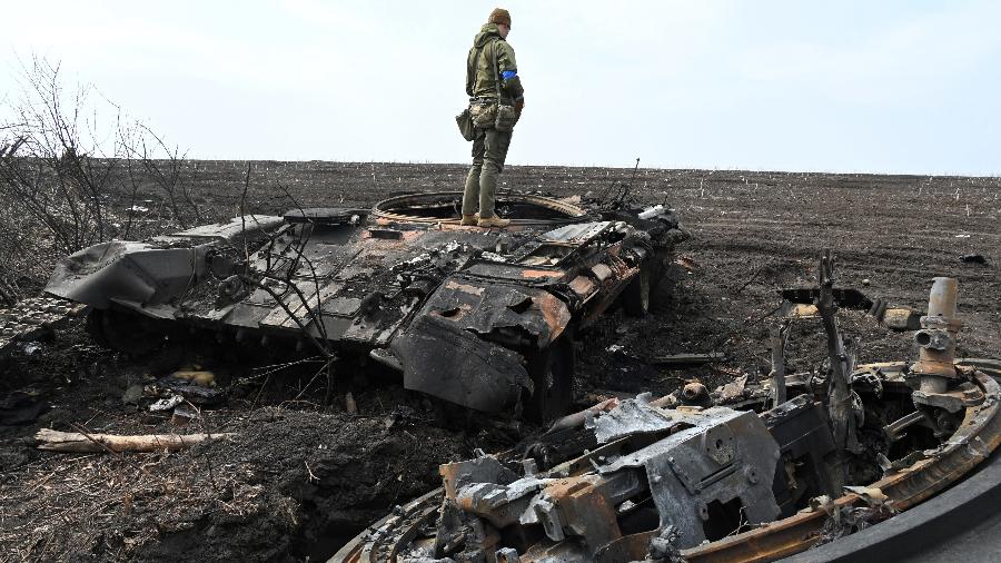 01.abr.2022/ Um soldado ucraniano sobre os destroços de um tanque russo queimado fora da vila de Mala Rogan, a leste de Kharkiv - SERGEY BOBOK / AFP