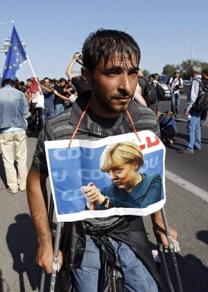 Refugiado usa imagem de Angela Merkel pendurada no pescoço - Zsolt Szigetvary/EFE