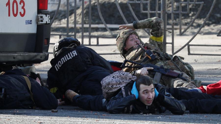 26.fev.22 - Em Kiev, pessoas tapam os ouvidos e se protegem após sirene de alerta soar próximo a prédio destruído - Gleb Garanich/Reuters