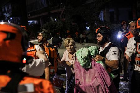 15.6.2025 - Equipes de resgate e segurança ajudam uma mulher ferida no local do impacto após ataque com mísseis do Irã contra Israel, no centro de Israel 15.6.2025 - Equipes de resgate e segurança ajudam uma mulher ferida no local do impacto após ataque com mísseis do Irã contra Israel, no centro de Israel