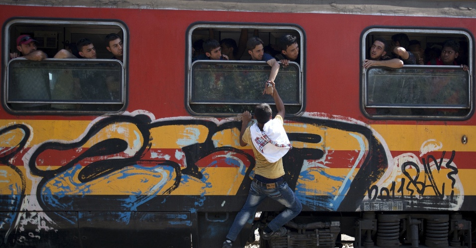 15.ago.2015 - Imigrante é segurado por outro do lado de foram de um trem na estação de Gevgelija, na Macedônia, perto da fronteira com a Grécia