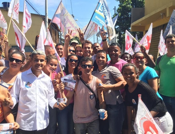 Mendes (centro, fazendo 'V' de vitória) faz campanha em meio a populares, que mostram santinhos, adesivos e bandeiras de candidatos de PPS, PTN e PMDB em Cabo Frio (RJ)