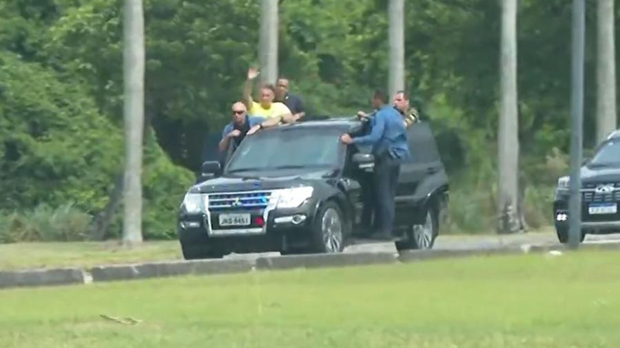 Bolsonaro acena com o corpo para fora de carro em movimento - Reprodução/TV Globo