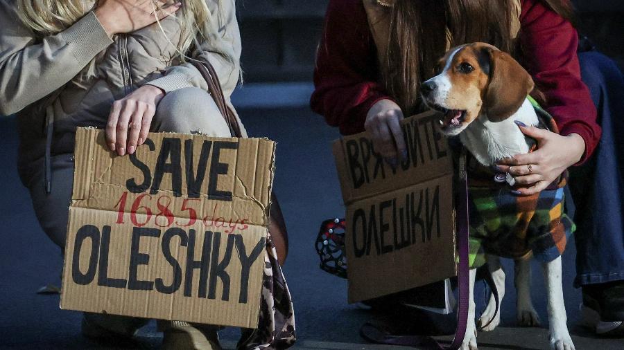 Um cachorro observa enquanto mulheres seguram cartazes durante uma manifestação pedindo a criação de um corredor humanitário para retirar civis ucranianos da cidade de Oleshky, na região de Kherson6 de outubro de 2026REUTERS/Alina Smutko