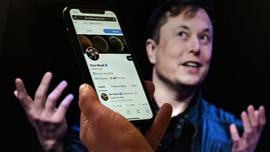 Celular exibe perfil de Elon Musk no Twitter; ao fundo, uma foto do bilionário e dono da rede social - Olivier Douliery/AFP