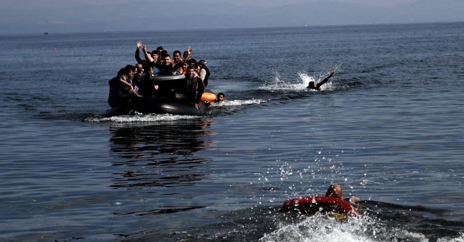 27.set.2015 - Refugiados acenam ao se aproximar da ilha grega de Lesbos neste domingo (27). Eles saíram de barco da Turquia e cruzaram o mar Egeu. Na mesma travessia, 17 sírios, incluindo cinco mulheres e cinco crianças, morreram afogados quando o barco em que viajavam naufragou, segundo a agência de notícias turca Dogan