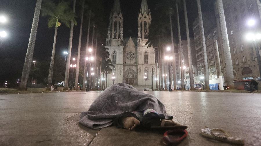 Morador de rua se abriga do frio enquanto dorme durante a madrugada frente da Catedral da Sé, no centro de São Paulo - Alex Silva/Estadão Conteúdo