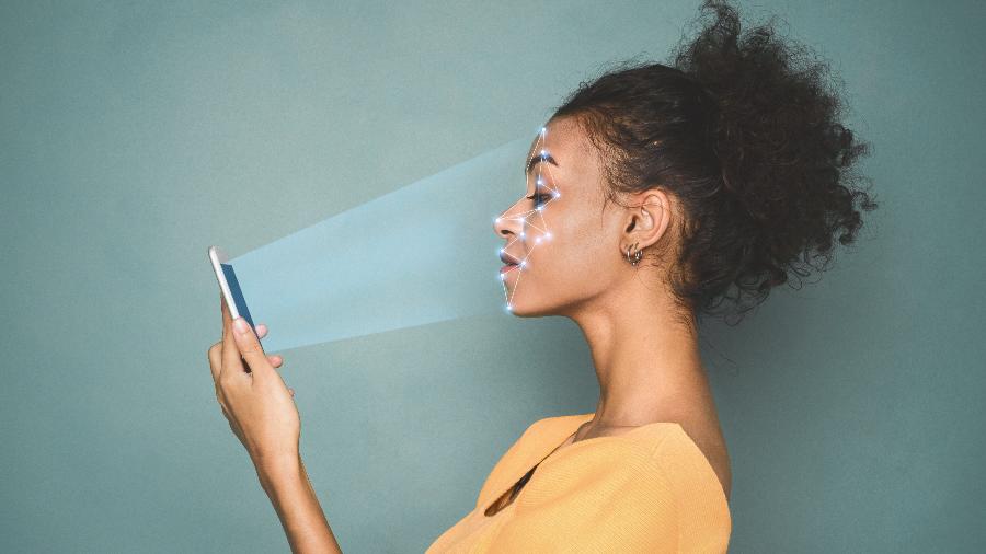 Mulher olhando smartphone com tecnologia de reconhecimento facial - iStock