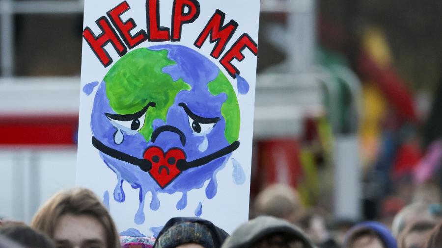 Cartaz empunhado por manifestante em protesto durante a COP26 mostra o planeta Terra pedindo socorro - Yves Herman/Reuters