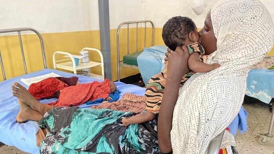Hawa segura sua filha Ubah ao lado da cama onde seu filho Abdiwali está deitado - BBC/ ED HABERSHON
