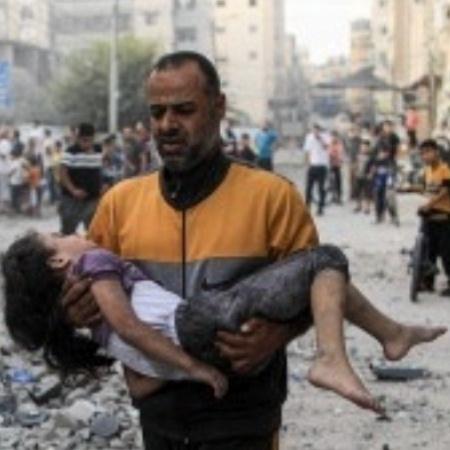 Homem leva criança nos braços após bombardeios na Faixa de Gaza