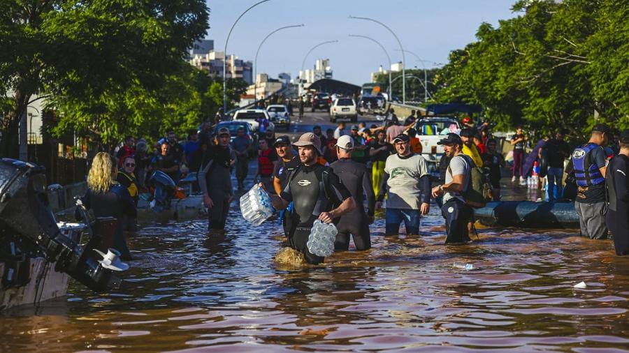 6.mai.2024 - Voluntários caminham por rua alagada na cidade de Porto Alegre; estado do Rio Grande do Sul foi atingido por fortes chuvas nos últimos dias