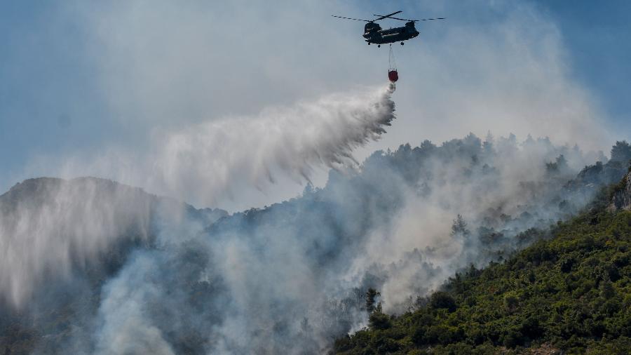 Helicóptero despeja água sobre área incendiada em uma floresta próximo a Malakasa, ao norte de Atenas (Grécia) - Louisa Gouliamaki/AFP