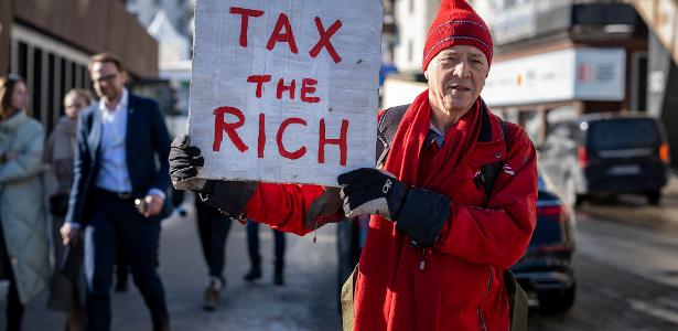 O milionário britânico Phil White segura um cartaz onde se lê: 'Taxe os ricos' ao lado do Centro de Congressos durante o Fórum Econômico Mundial
