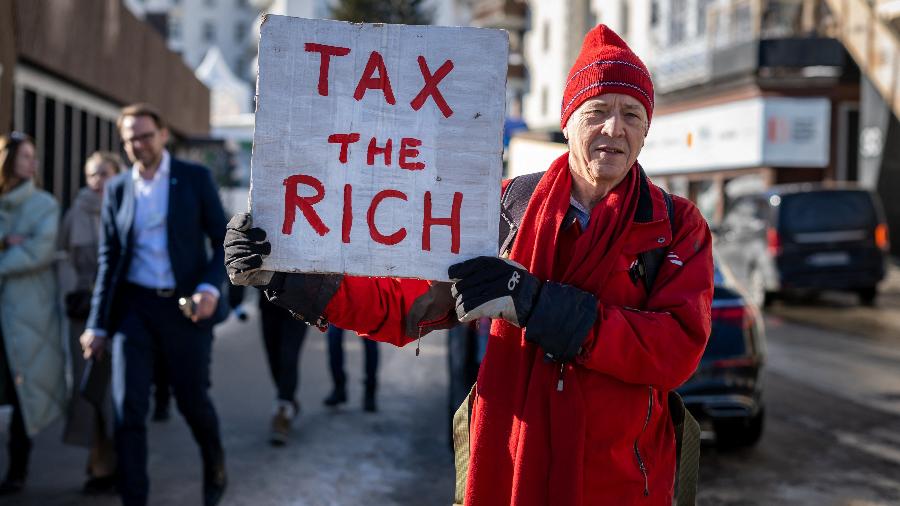 O milionário britânico Phil White segura um cartaz onde se lê: "Taxe os ricos" durante o Fórum Econômico Mundial - Fabrice COFFRINI/AFP