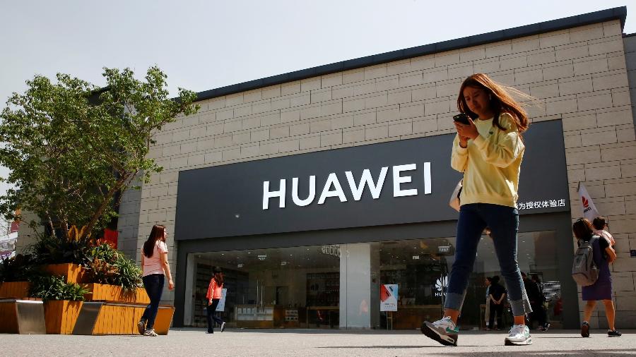 Mulher olha para o telefone enquanto passa por uma loja da Huawei em Pequim, China - Thomas Peter/Reuters