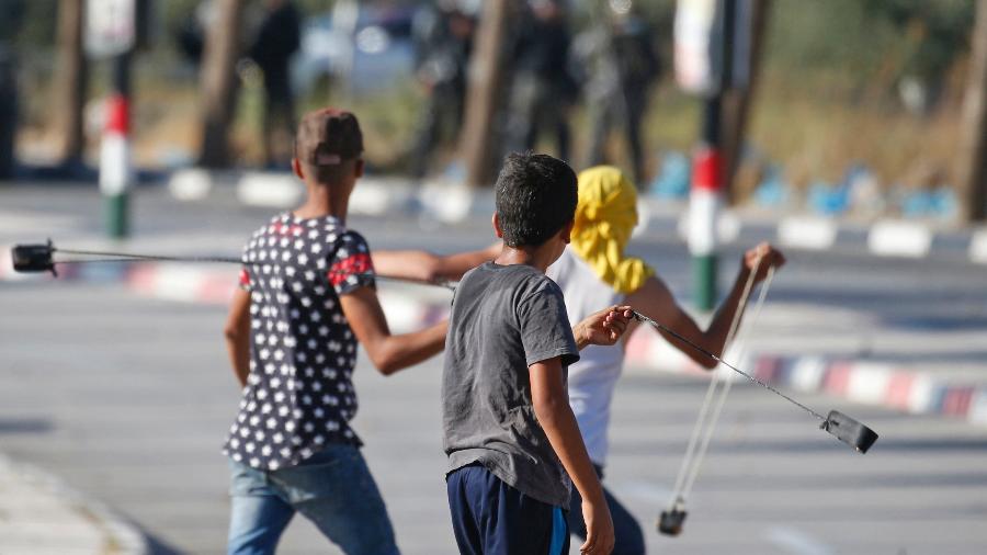 Jovens palestinos arremessam pedras na direção do exército israelense durante protesto - JAAFAR ASHTIYEH