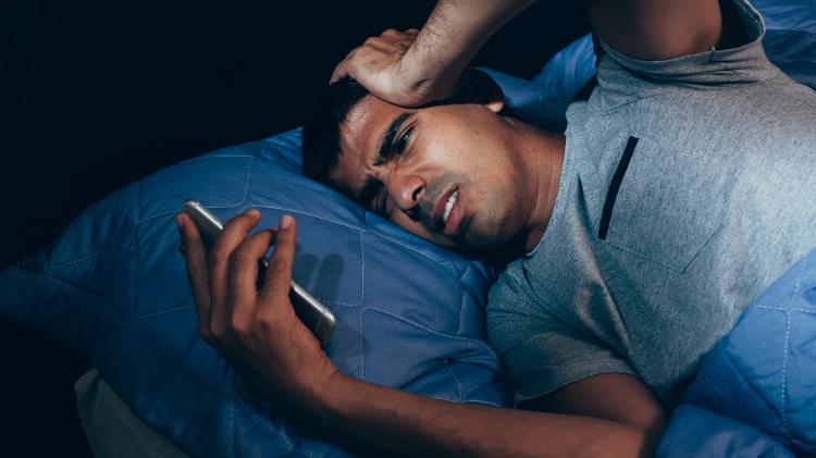 Homem acordando no meio da noite por uma chamada no celular Homem acordando no meio da noite por uma chamada no celular