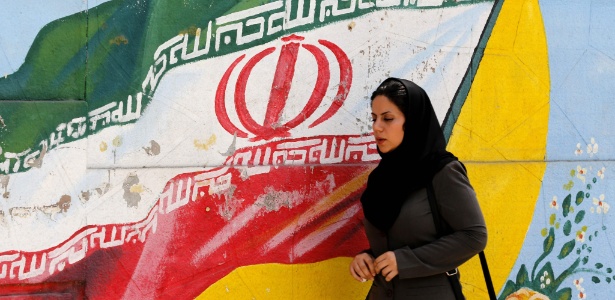 Mulher passa em frente a pintura com bandeira do Irã em Teerã