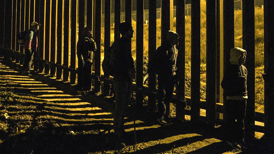 Migrantes em Tijuana, no México, observam agentes da Patrulha da Fronteira dos Estados Unidos do outro lado da cerca - Mauricio Lima/The New York Times