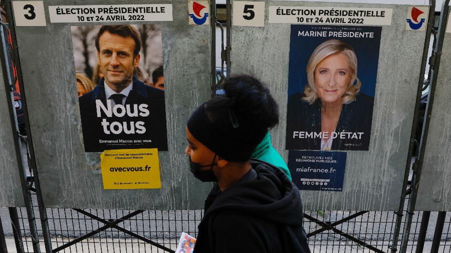 4.abr.2022 - Pessoas passam em frente a cartazes das campanhas de Emmanuel Macron e Marine le Pen, candidatos na eleição presidencial da França, exibidos na capital, Paris - 4.abr.2022 - Gonzalo Fuentes/Reuters