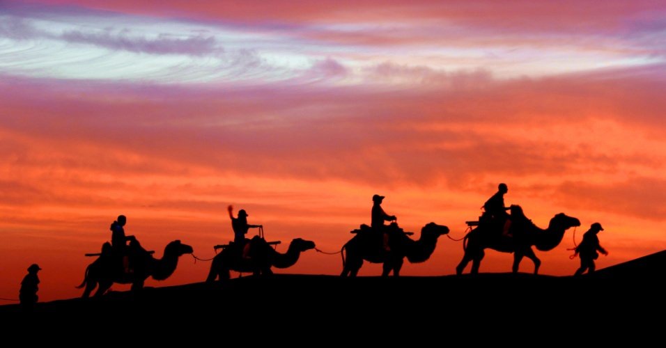 28.jul.2015 - Turistas montam em camelos ao amanhecer durante passeio na colina Mingsha, em Dunhuang (China)