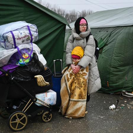 Mulher que fugiu da Ucrânia abraça uma menina enrolada em um cobertor na frente de uma barraca depois de cruzar o posto de controle da fronteira entre a Moldávia e a Ucrânia - NIKOLAY DOYCHINOV/AFP