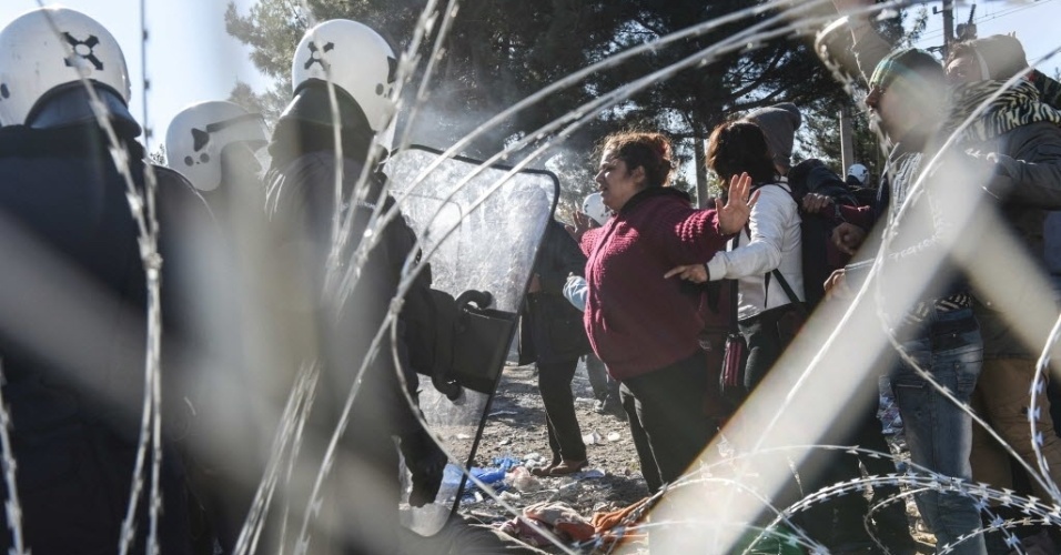 3.dez.2015 - Mulher abre os braços em frente a policiais enquanto imigrantes tentam cruzar a fronteira entre a Grécia e a Macedônia, no vilarejo grego de Idomeni