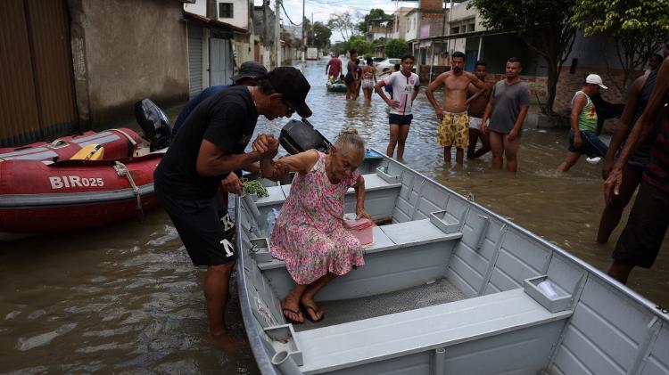 Morador ajuda idosa a deixar barco após deixar sua casa que foi alagada em Duque de Caxias, no Rio de Janeiro