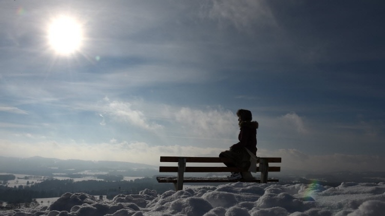 20.jan.2016 - Jovem sentada em banco em local coberto de neve com Sol ao fundo parece "flutuar nas nuvens". A foto foi feita em região montanhosa de Irschenberg, na Alemanha - Christof Stache/AFP - Christof Stache/AFP