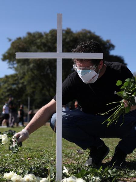 Homem coloca flores perto de uma cruz durante um protesto e tributo aos profissionais de saúde mortos por coronavírus em São Paulo - Amanda Perobelli/Reuters