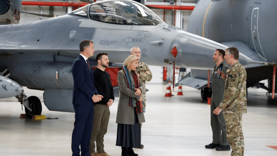 O presidente ucraniano Volodymyr Zelensky, o primeiro-ministro belga Alexander De Croo e a ministra da Defesa belga Ludivine Dedonder ao lado de um F-16 enquanto se reúnem com instrutores na base aérea de Melsbroek, perto de Bruxelas, Bélgica, na última terça-feira (28) - Piroschka Van De Wouw/Reuters via RFI