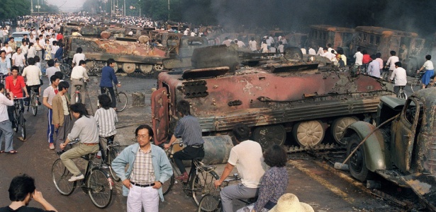 Imagem de 4 de junho de 1989 mostra moradores de Pequim passando por veículos militares queimados por manifestantes durante os confrontos na Praça da Paz Celestial - Manny Ceneta/ AFP