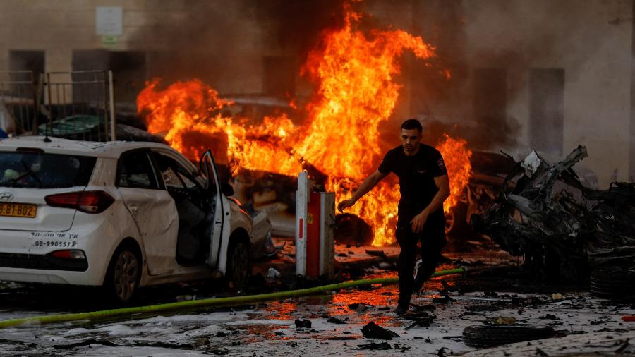 Homem corre perto de carro em chamas após o lançamento de foguetes da Faixa de Gaza, em Israel