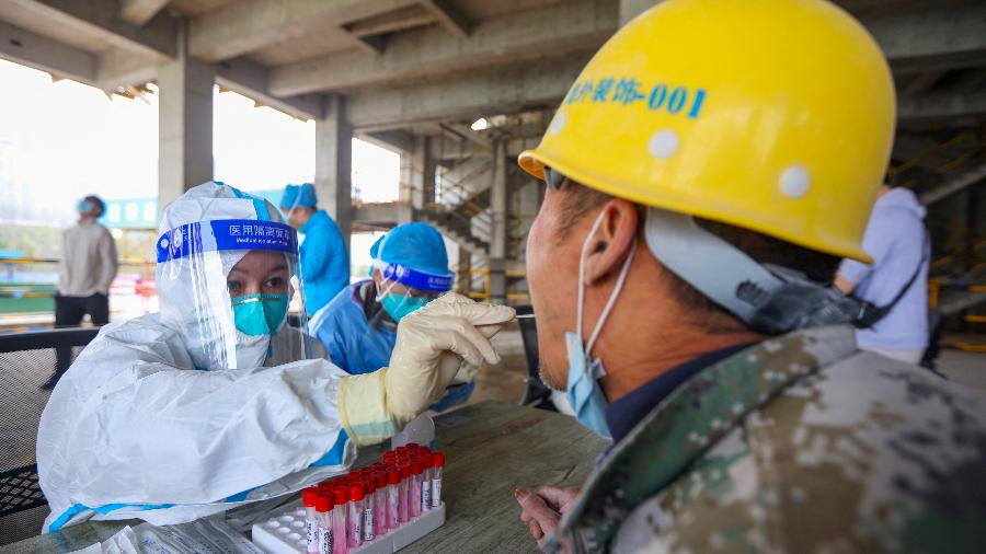 Um trabalhador médico em traje de proteção coleta uma amostra de cotonete de um trabalhador em um canteiro de obras após casos da doença de coronavírus em Nanjing, província de Jiangsu, China, 23 de março de 2022 - Stringer/via Reuters